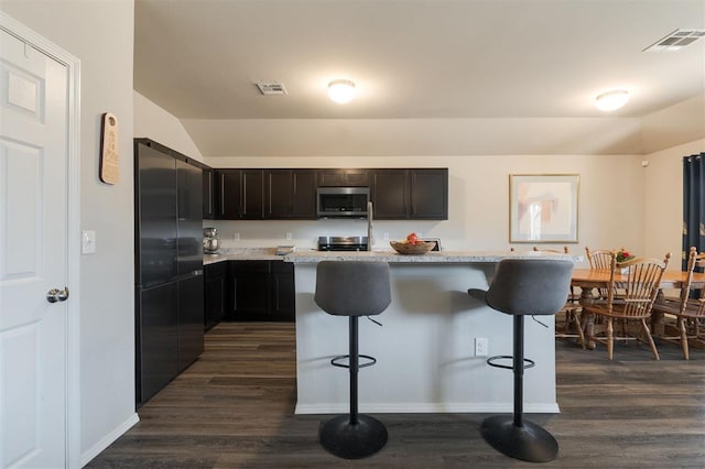 kitchen featuring appliances with stainless steel finishes, visible vents, dark wood-type flooring, and a kitchen breakfast bar