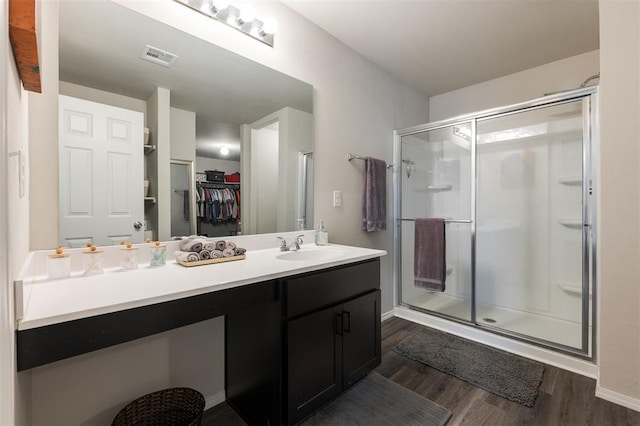 full bathroom featuring a walk in closet, visible vents, a stall shower, vanity, and wood finished floors