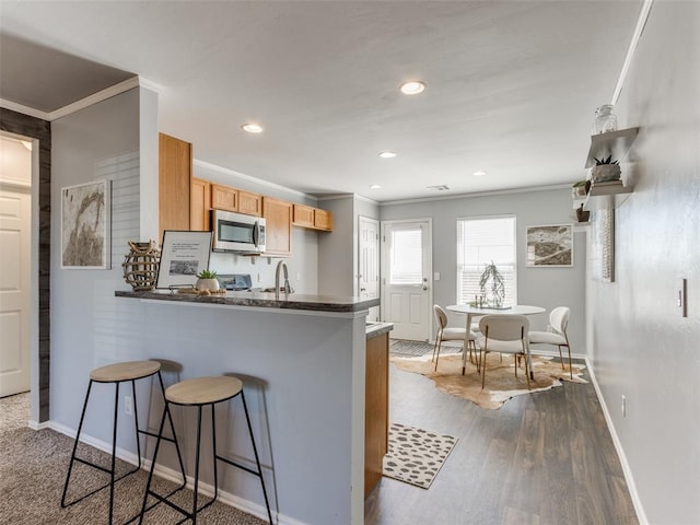 kitchen with dark wood-style floors, crown molding, a breakfast bar area, stainless steel microwave, and a peninsula