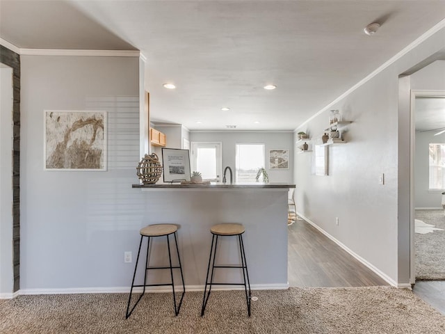 kitchen featuring a kitchen bar, dark carpet, ornamental molding, a peninsula, and baseboards