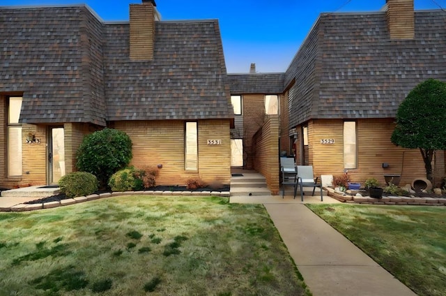 back of house with a yard, mansard roof, roof with shingles, and a chimney