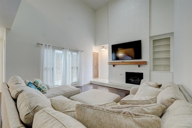 living area featuring a high ceiling, a fireplace, built in features, and wood finished floors