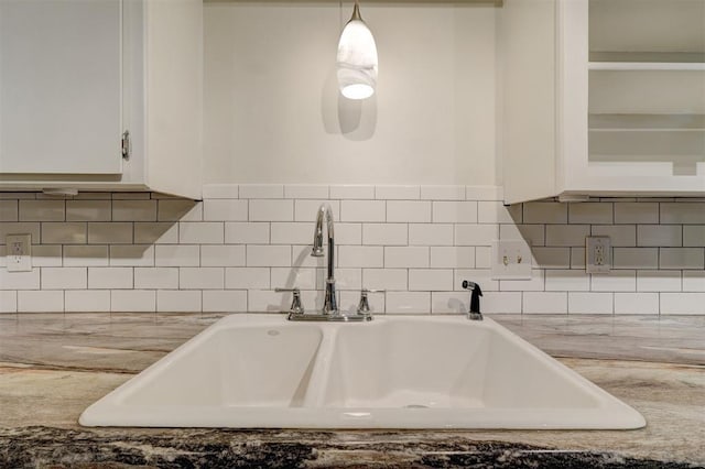 interior space featuring tasteful backsplash, glass insert cabinets, a sink, and white cabinetry