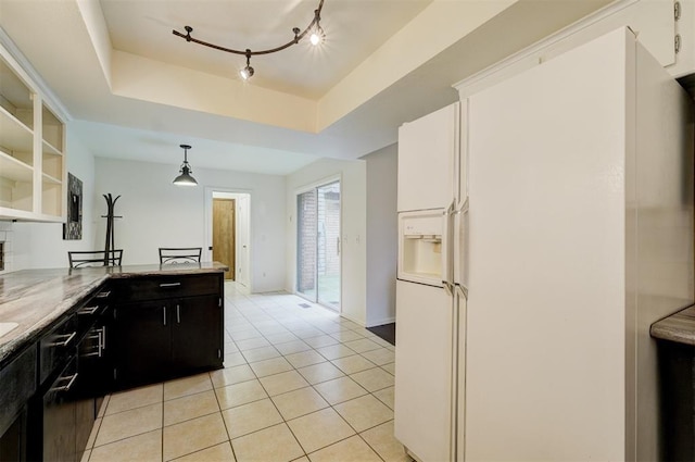 kitchen with light tile patterned floors, white refrigerator with ice dispenser, hanging light fixtures, a tray ceiling, and dark cabinetry