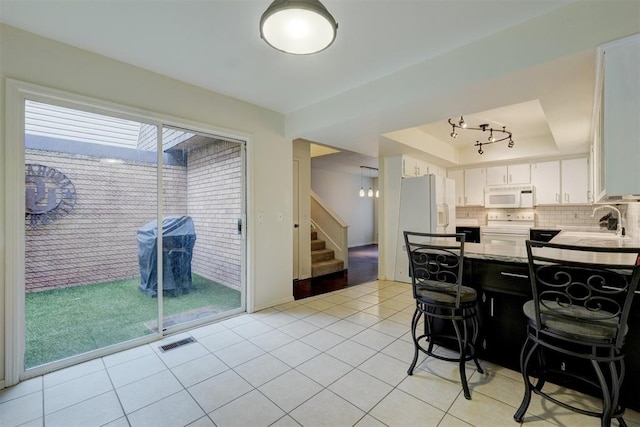 kitchen featuring tasteful backsplash, a raised ceiling, visible vents, light tile patterned flooring, and white appliances