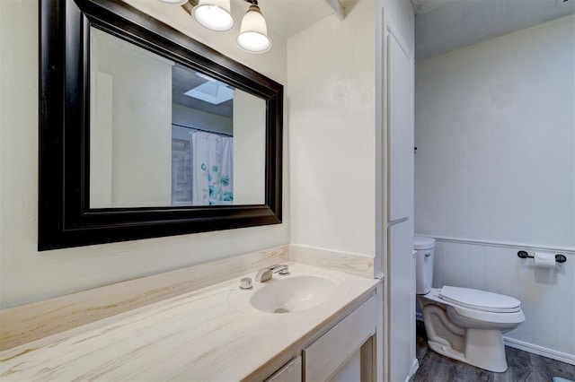 bathroom with toilet, a wainscoted wall, wood finished floors, and vanity