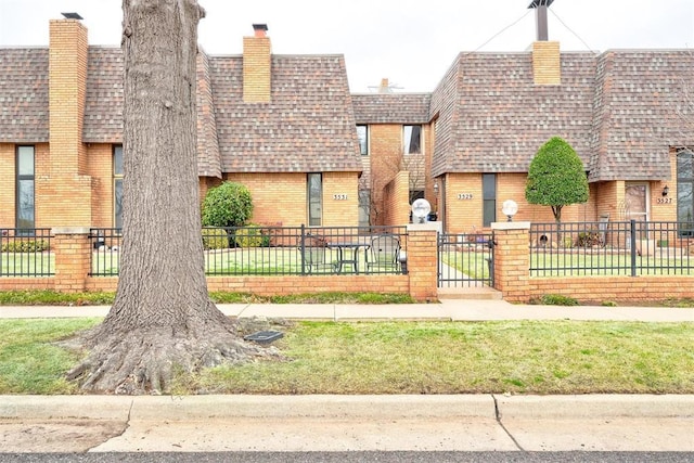 view of front of house with a shingled roof, brick siding, and a fenced front yard