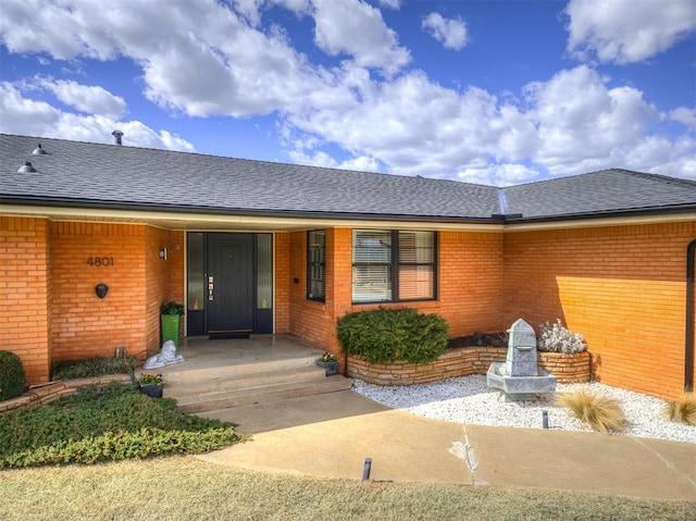 entrance to property with covered porch, brick siding, and roof with shingles