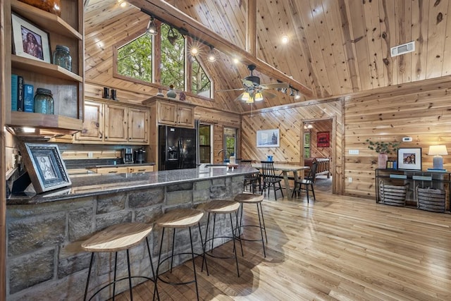 kitchen featuring black refrigerator with ice dispenser, wood ceiling, a sink, wooden walls, and high vaulted ceiling