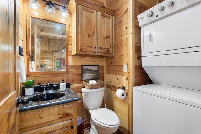 half bathroom with wooden walls, vanity, toilet, and stacked washer / drying machine