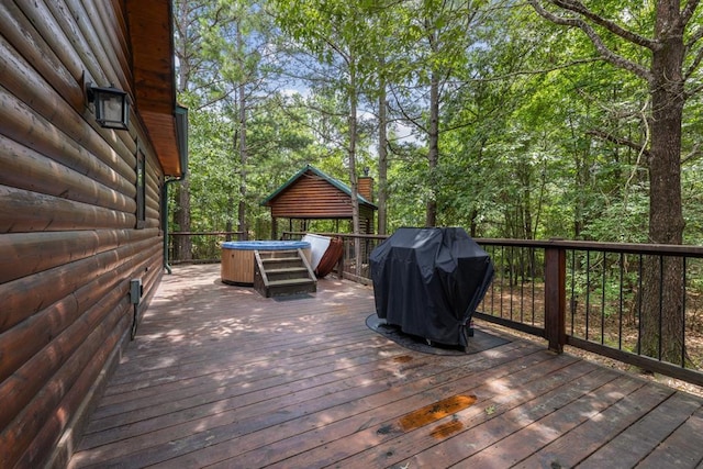 deck with a grill, a hot tub, and a wooded view