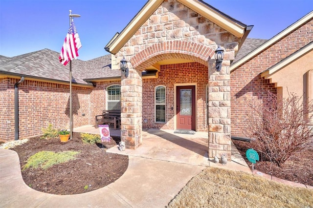 view of exterior entry featuring stone siding, roof with shingles, and brick siding