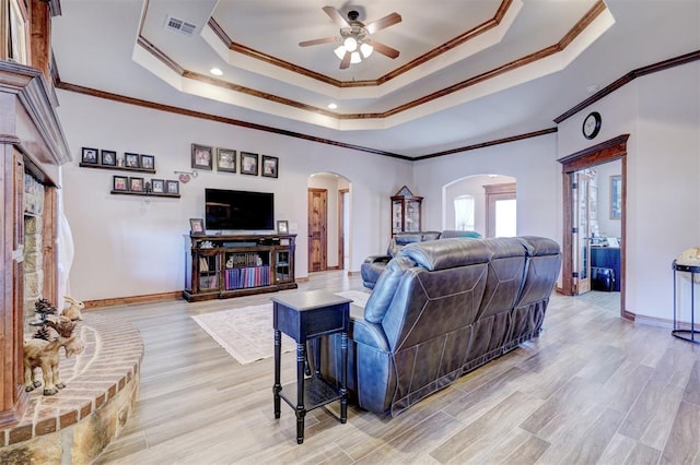 living area featuring arched walkways, a tray ceiling, light wood-type flooring, and visible vents