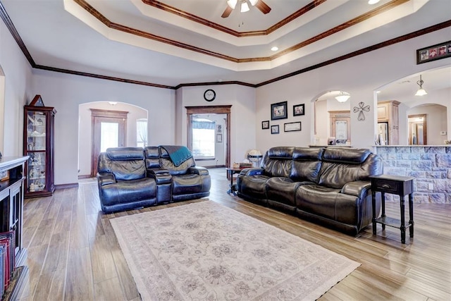 living area featuring light wood finished floors, baseboards, a tray ceiling, and crown molding