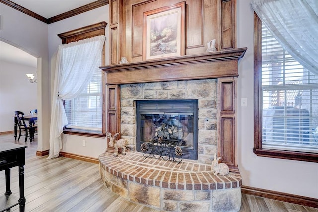 living area featuring arched walkways, light wood-style flooring, ornamental molding, a glass covered fireplace, and baseboards