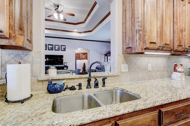 kitchen featuring light stone countertops, a sink, backsplash, brown cabinets, and crown molding