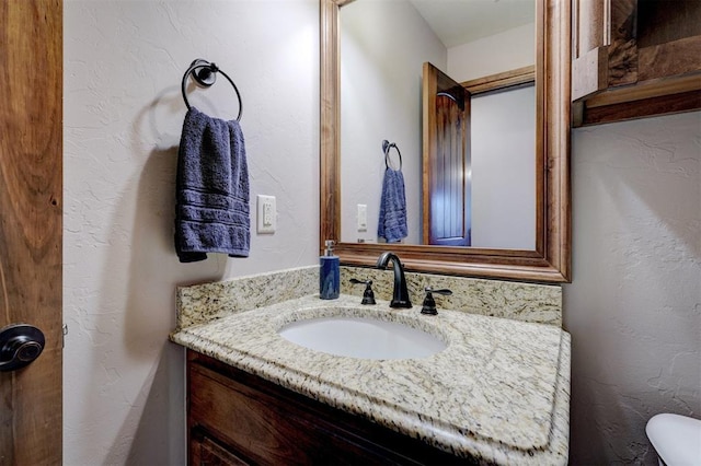 half bath with toilet, a textured wall, and vanity