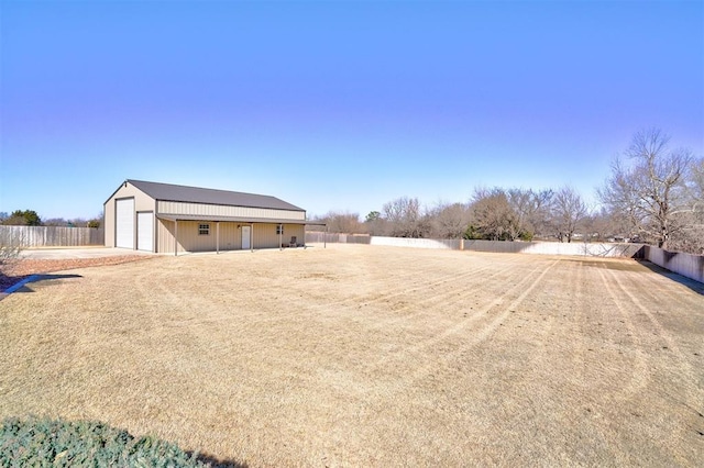 view of yard with driveway, a detached garage, fence, and an outdoor structure