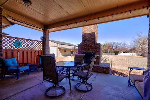 view of patio featuring an outbuilding, an outdoor brick fireplace, outdoor dining space, and fence