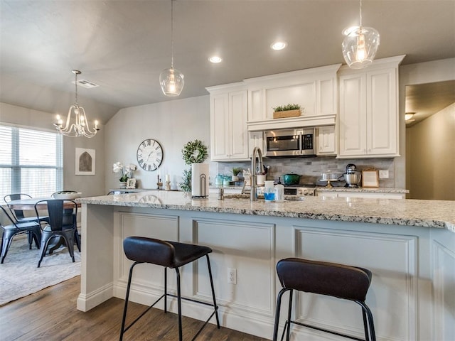 kitchen featuring dark wood finished floors, stainless steel microwave, light stone countertops, white cabinetry, and backsplash