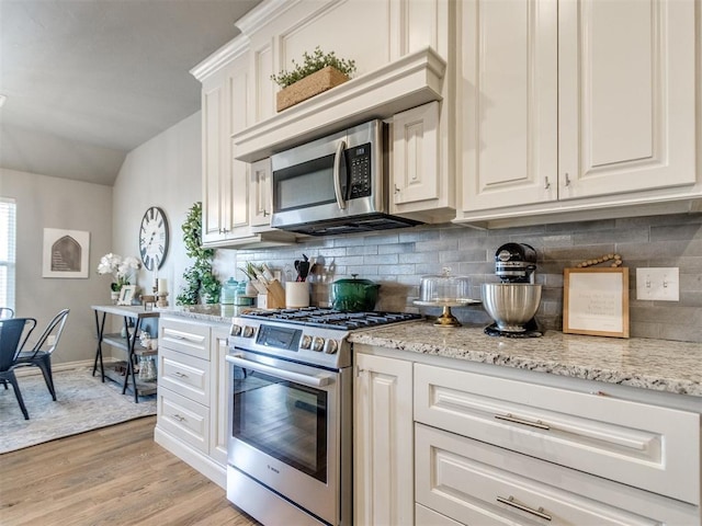 kitchen featuring light stone counters, light wood-style flooring, decorative backsplash, appliances with stainless steel finishes, and white cabinetry