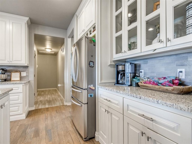 kitchen featuring backsplash, light wood-style flooring, freestanding refrigerator, white cabinets, and light stone countertops