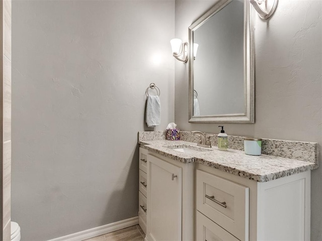 half bath featuring toilet, wood finished floors, vanity, and baseboards