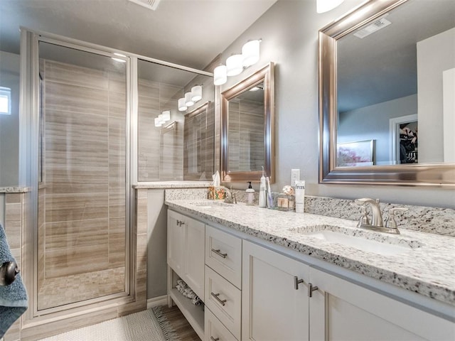 bathroom featuring double vanity, a stall shower, a sink, and visible vents