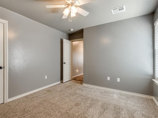 carpeted spare room with visible vents, ceiling fan, and baseboards