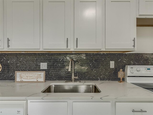 kitchen featuring tasteful backsplash, stove, white cabinetry, a sink, and light stone countertops