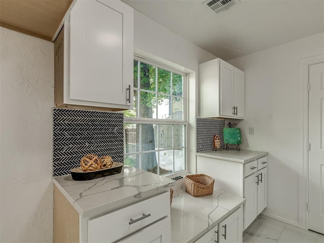 kitchen with visible vents, decorative backsplash, light stone counters, marble finish floor, and white cabinetry