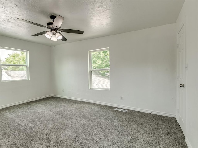 empty room with a healthy amount of sunlight, a textured ceiling, visible vents, and carpet flooring