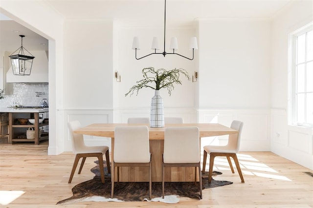 dining space with crown molding, light wood-type flooring, plenty of natural light, and an inviting chandelier