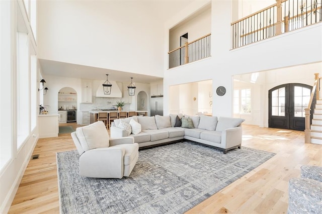 living room featuring light wood-style floors, arched walkways, french doors, and visible vents