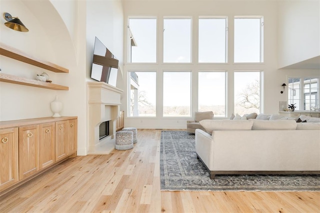 living area with a wealth of natural light, a glass covered fireplace, light wood-style flooring, and a towering ceiling