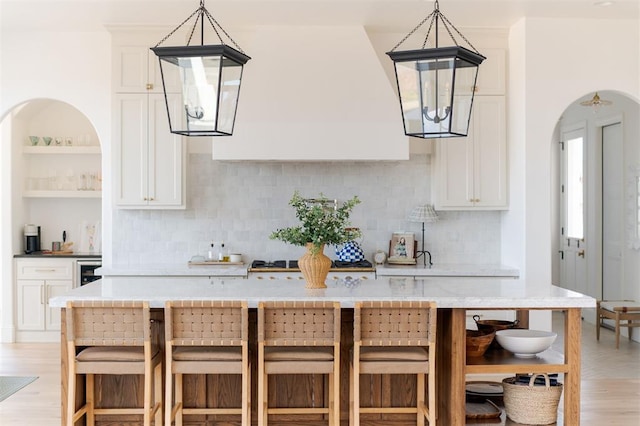 kitchen featuring arched walkways, light wood-style flooring, a kitchen breakfast bar, and open shelves