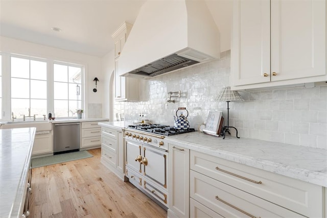 kitchen featuring gas cooktop, light wood-style flooring, premium range hood, a sink, and stainless steel dishwasher