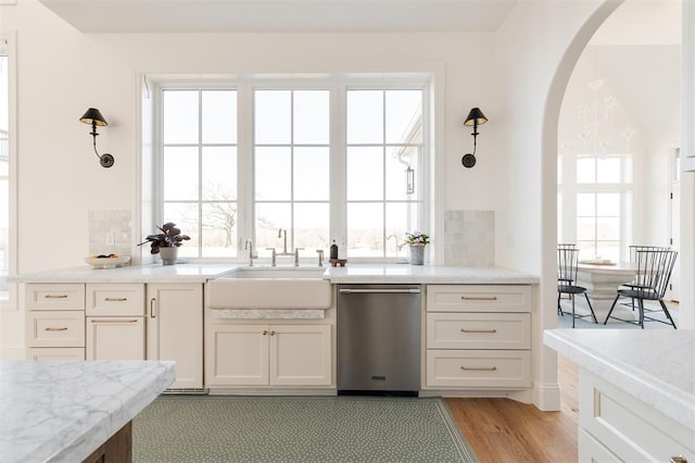 kitchen with arched walkways, dishwasher, light wood-style flooring, light stone counters, and a sink