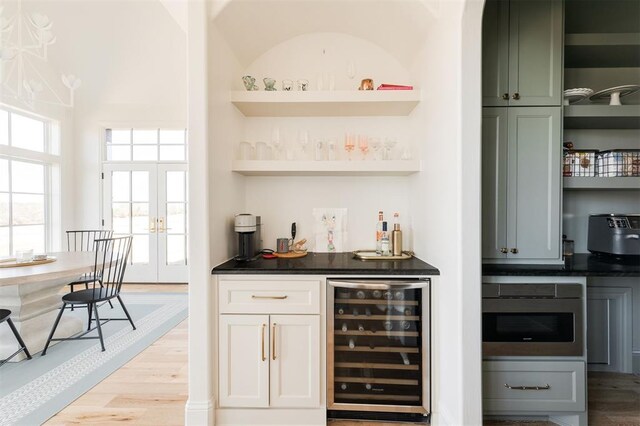 bar featuring beverage cooler, french doors, light wood finished floors, and a bar