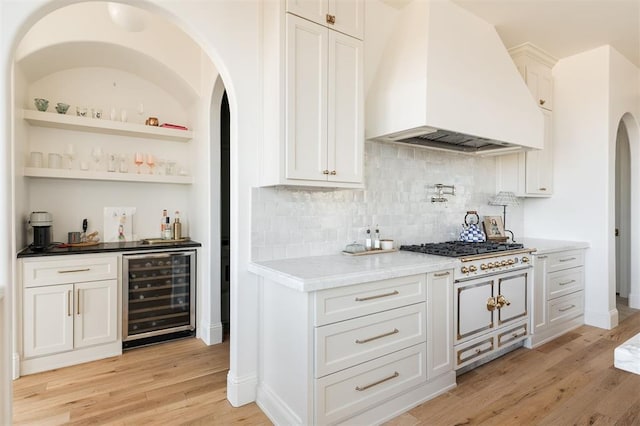 bar featuring beverage cooler, premium range hood, light wood-type flooring, decorative backsplash, and a dry bar