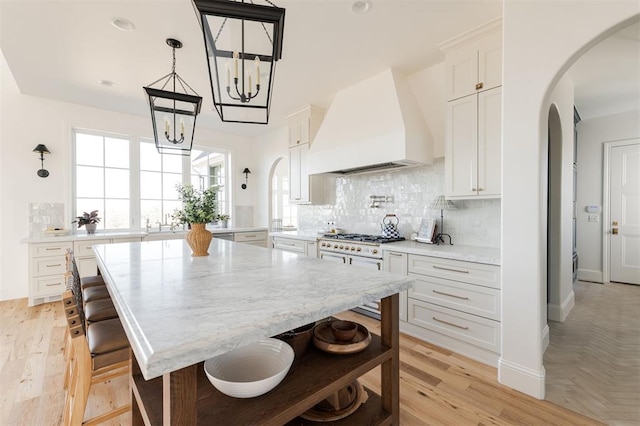 kitchen featuring premium range hood, white range with gas stovetop, arched walkways, and backsplash