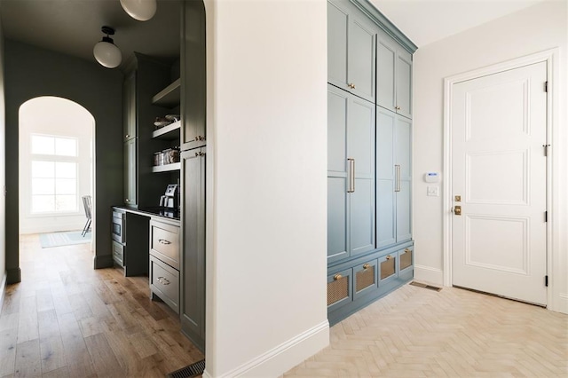 mudroom with arched walkways, light wood finished floors, visible vents, and baseboards