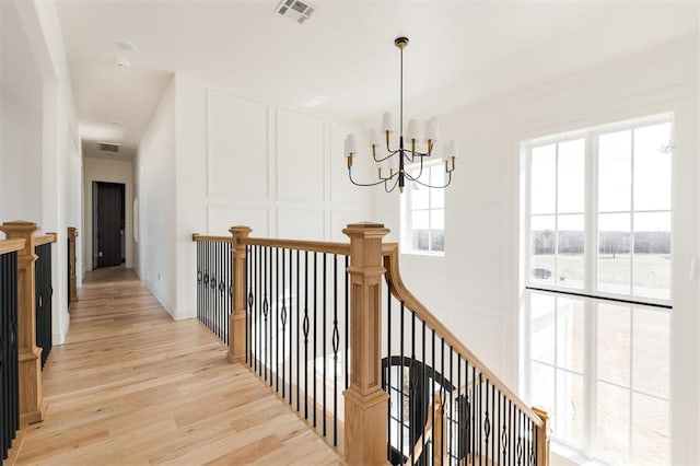 hallway with visible vents, a decorative wall, an inviting chandelier, an upstairs landing, and light wood-type flooring