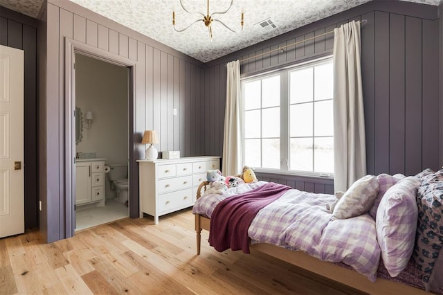 bedroom with a chandelier, a textured ceiling, connected bathroom, visible vents, and light wood-style floors