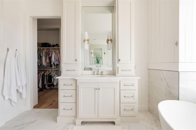 full bath with a walk in closet, marble finish floor, a freestanding tub, and vanity