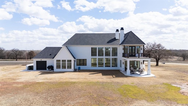 rear view of property with driveway, a garage, a balcony, a chimney, and stucco siding