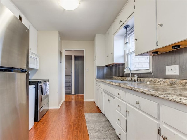 kitchen featuring light wood-style flooring, a sink, white cabinetry, appliances with stainless steel finishes, and backsplash