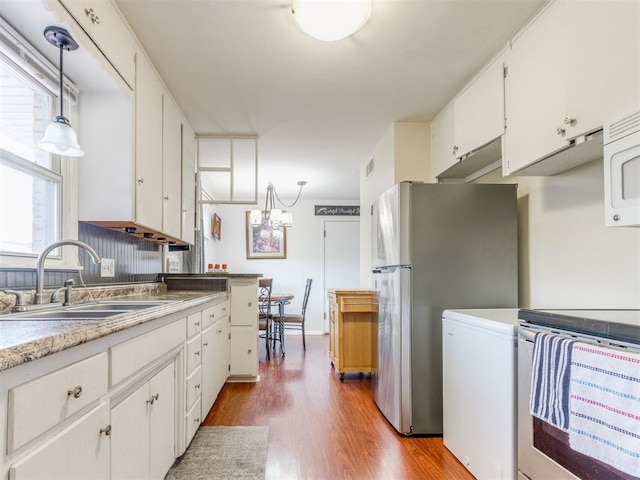 kitchen with decorative light fixtures, stainless steel appliances, light wood-style flooring, white cabinetry, and a sink