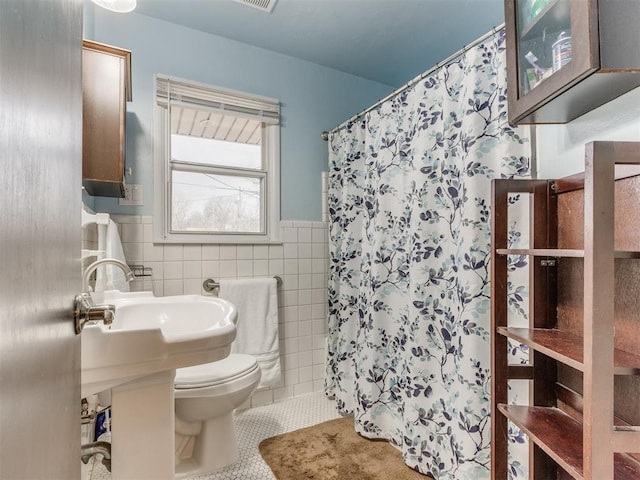 full bath featuring toilet, a wainscoted wall, a shower with curtain, tile patterned floors, and tile walls