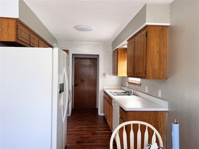 kitchen featuring white appliances, a sink, light countertops, dark wood-style floors, and brown cabinetry